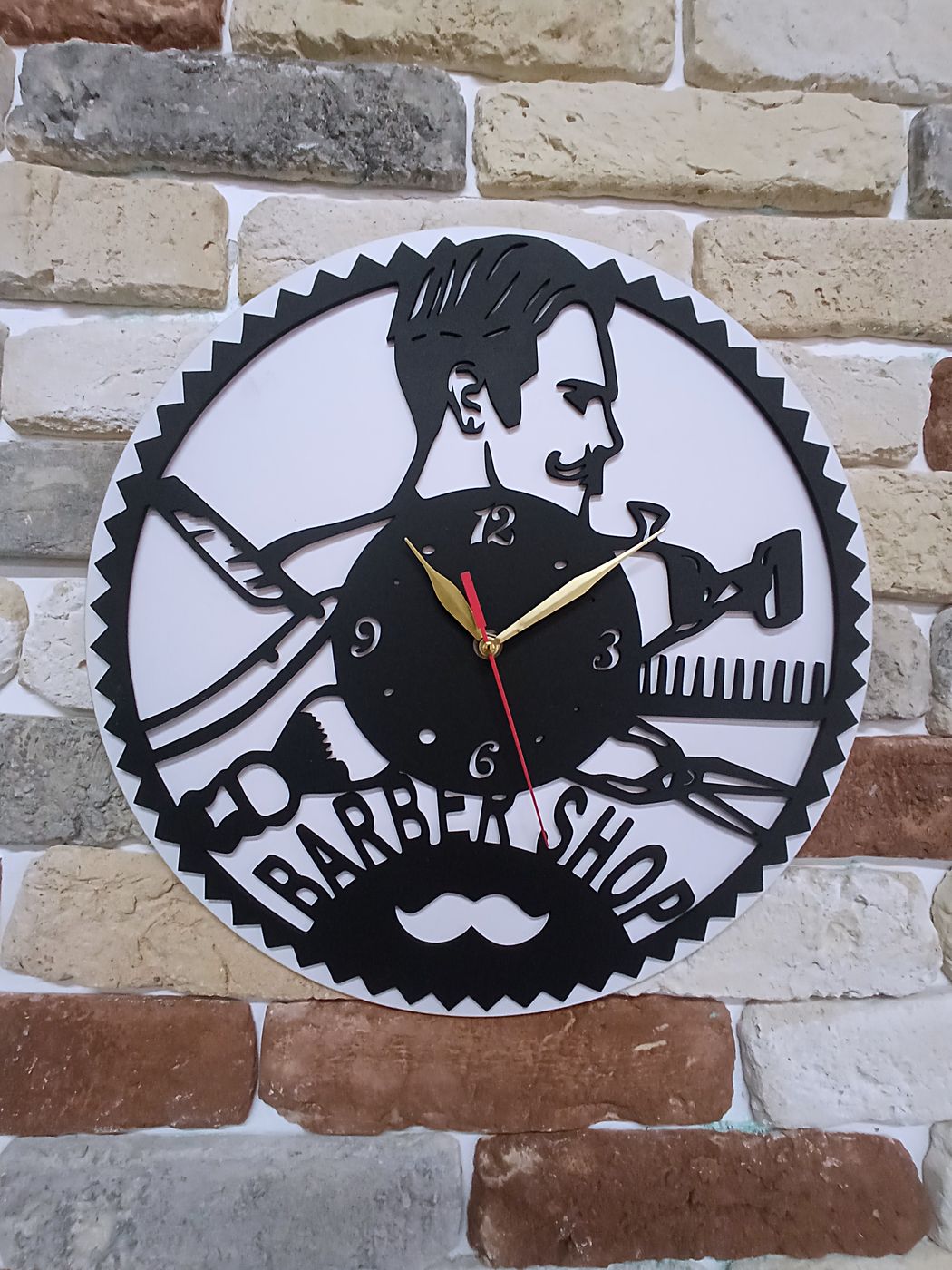 Чёрные часы Barber Shop на светлой кирпичной кладке, видны ножницы и расчёска