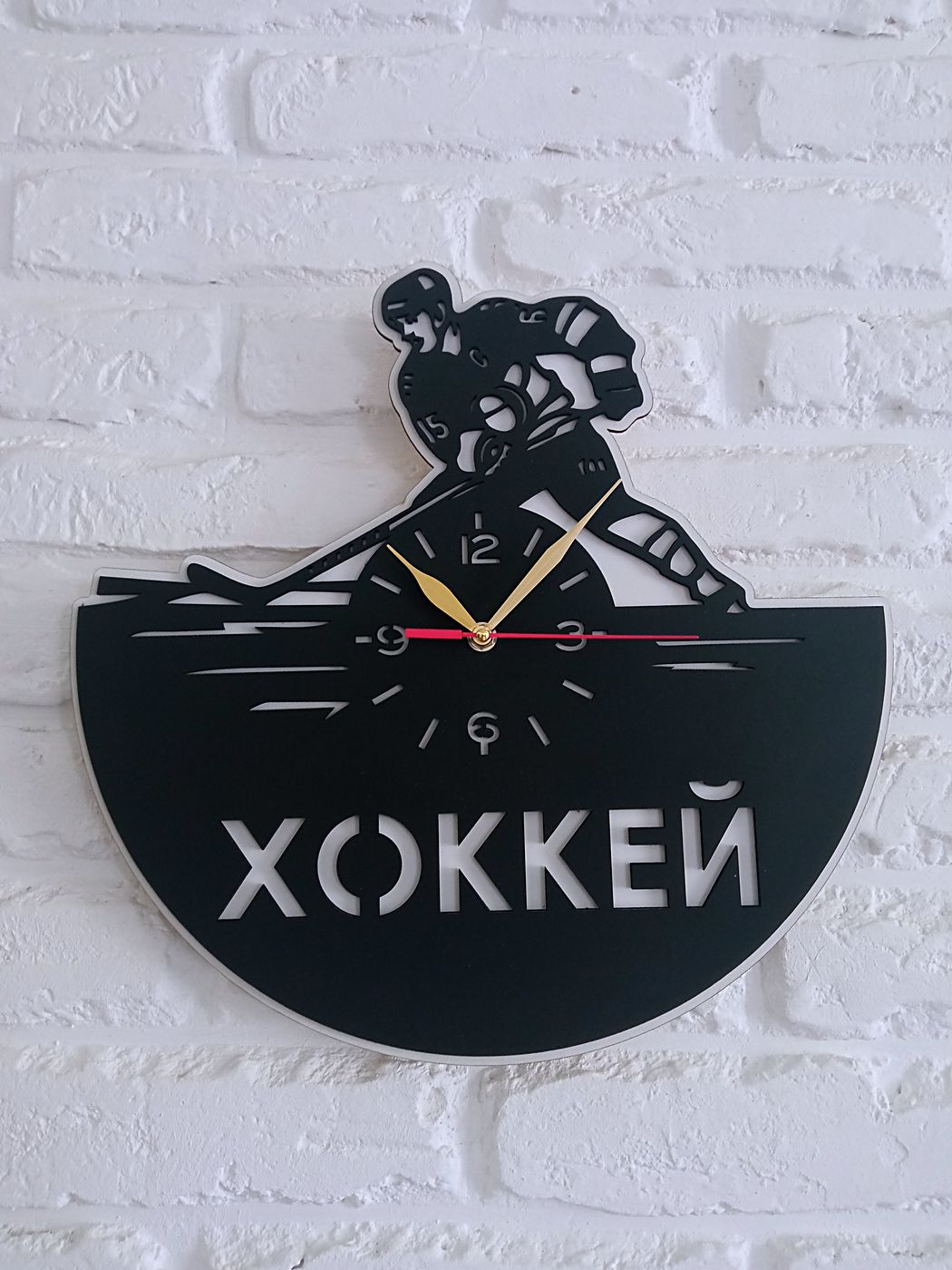 Часы «Хоккей» с силуэтом игрока над циферблатом на белой кирпичной стене