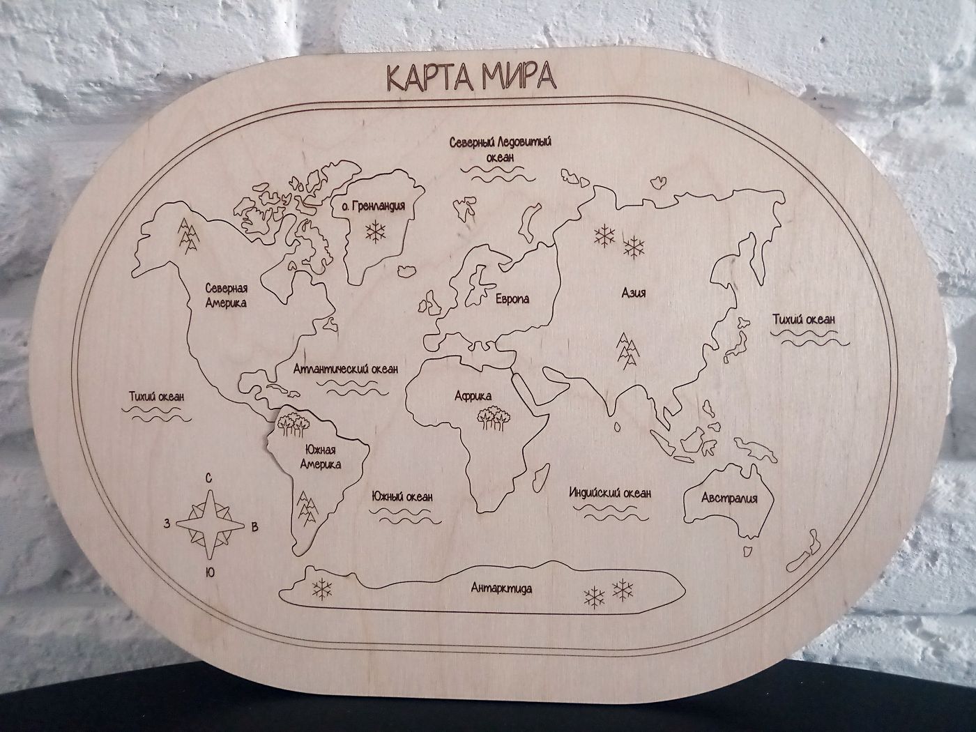 Деревянная карта мира на кирпичной стене: гравированные контуры материков и подписи