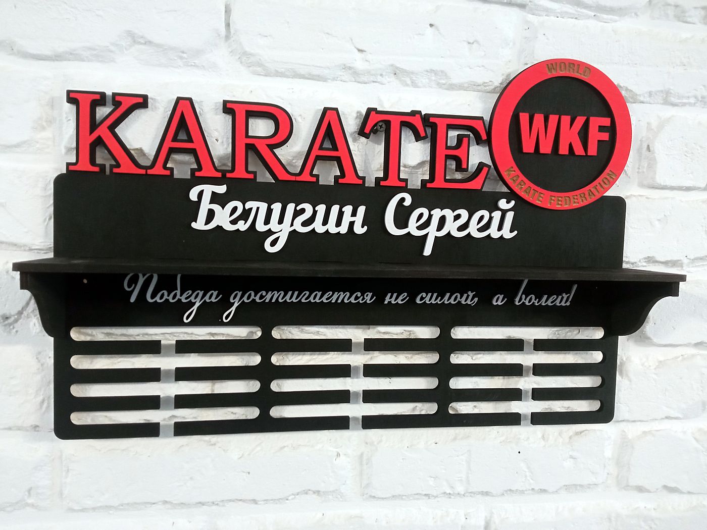 Чёрная медальница KARATE с эмблемой WKF и именем «Белугин Сергей» на белой стене