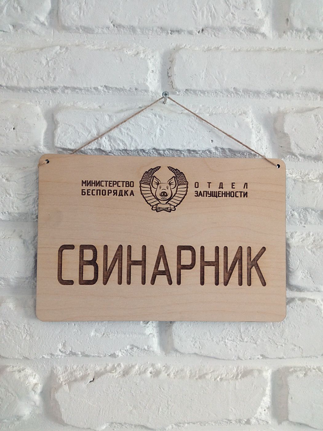 Деревянная табличка «Свинарник» на шнуре висит на белой кирпичной стене