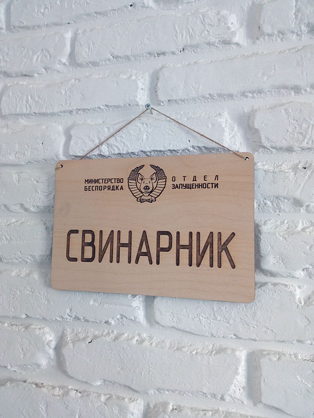 Табличка «Свинарник» под углом, виден шнур для подвеса и кромка фанеры